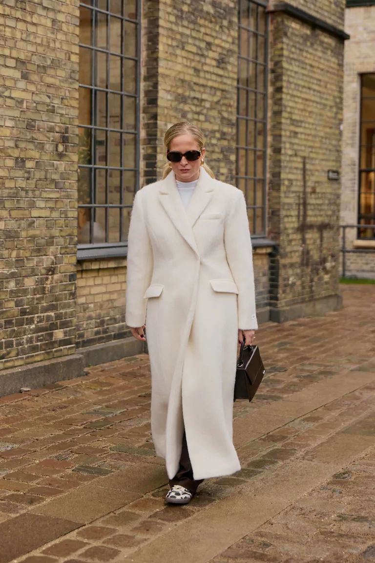 woman wearing cow-printed sneakers and a long white coat.