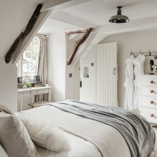 Bedroom in Unique Homestays x The White Company house, with beamed ceilings, bedspread, and robes hanging in the corner