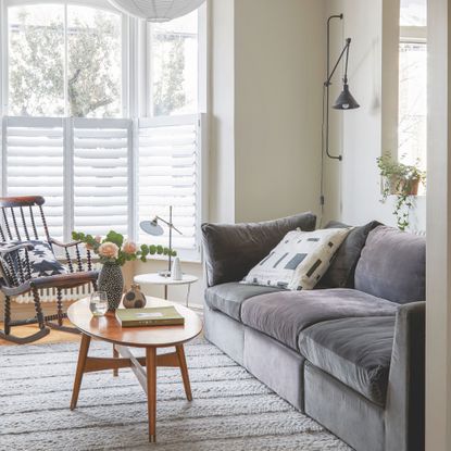 Neutral painted living room with shutters on the window, and a grey sofa on top of a cream rug
