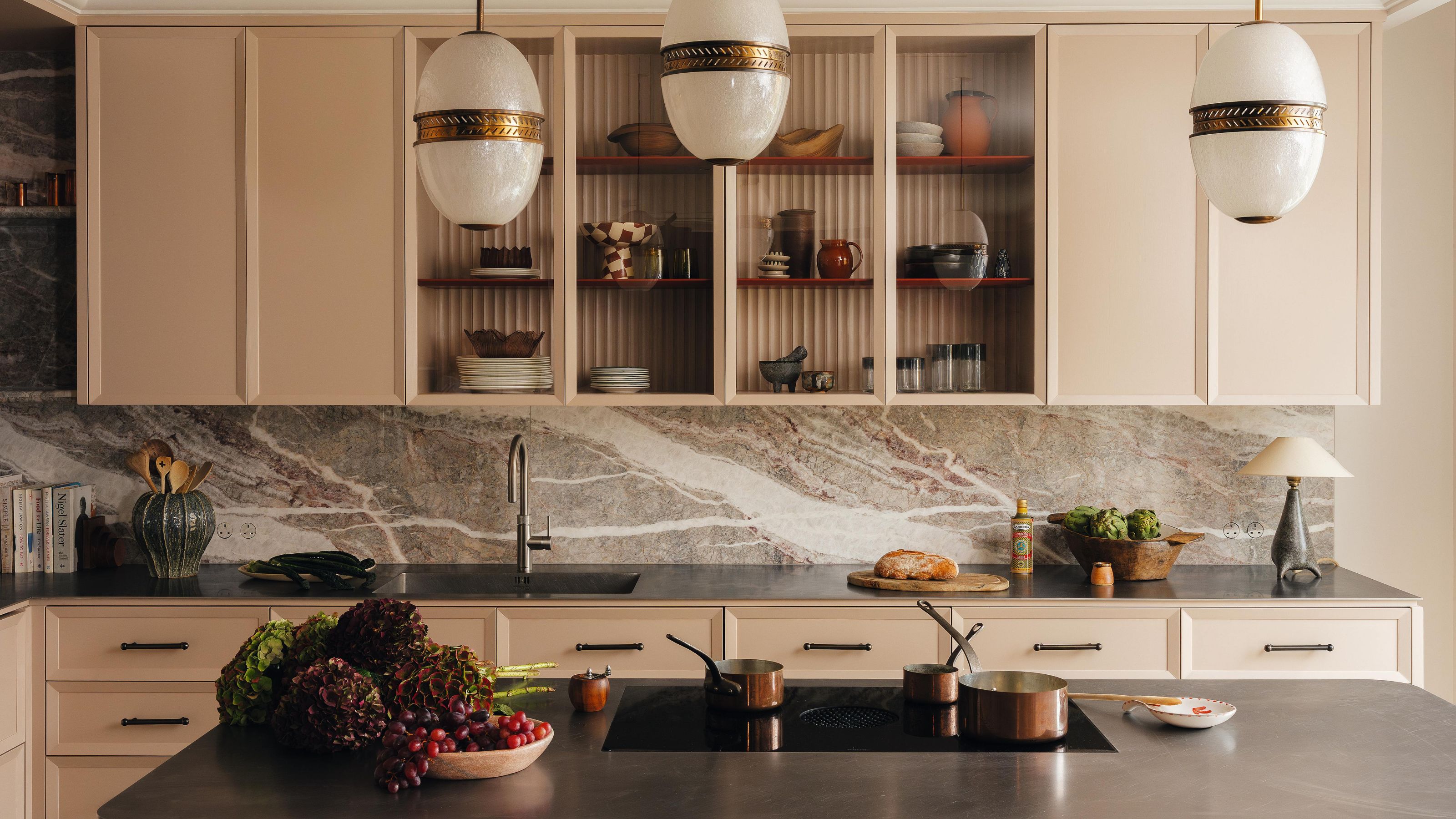 a pink modern kitchen with flat front cabinets with reeded glass upper units and a marble backsplash with a stainless stell island