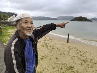 Local elder Kinsei Ishigaki points to the offshore crash site of McGrath's warplane in July 1945.