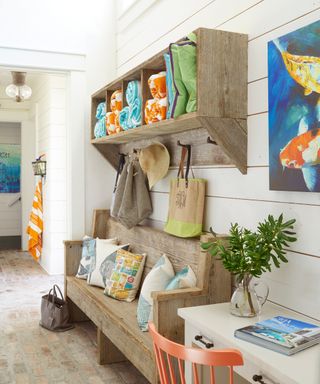 Beach vibes hallway with washed wood bench with scatter pillows, and matching wall hung wood shelf with cubby holes for beach towels, and hooks for bags and hats.