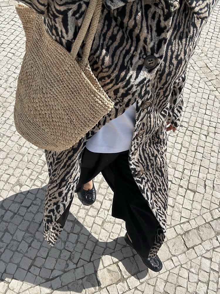 An image of @deborabrosa wearing a zebra-print coat with a raffia bag and ballet flats, some of the biggest fashion trends for spring 2026.