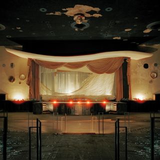 An abandoned theater with decaying decor is lit up by a red and goldeny light.