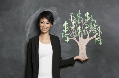 A woman stands with a chalk money tree drawing on a blackboard.