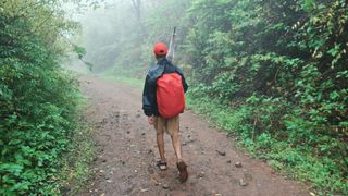 A man walks on a trail with a waterproof cover on his backpack