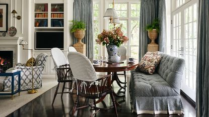 Blue-and-white breakfast room with a round wood table, mixed seating, striped curtains and garden-facing windows.
