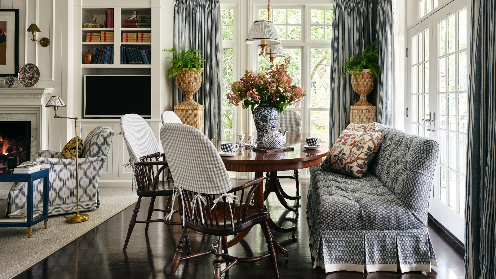 Blue-and-white breakfast room with a round wood table, mixed seating, striped curtains and garden-facing windows.