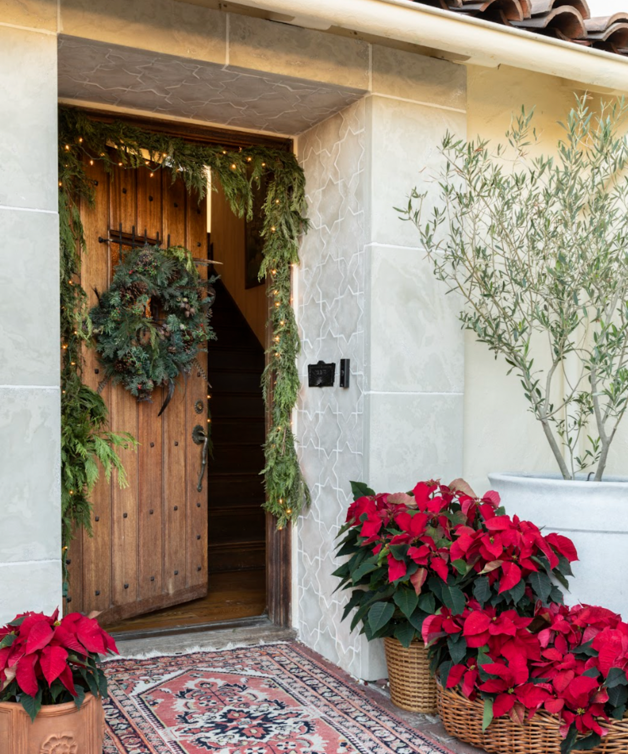 a front door entryway with poinsettias in baskets, garland around the door frame, and a wreath on the door