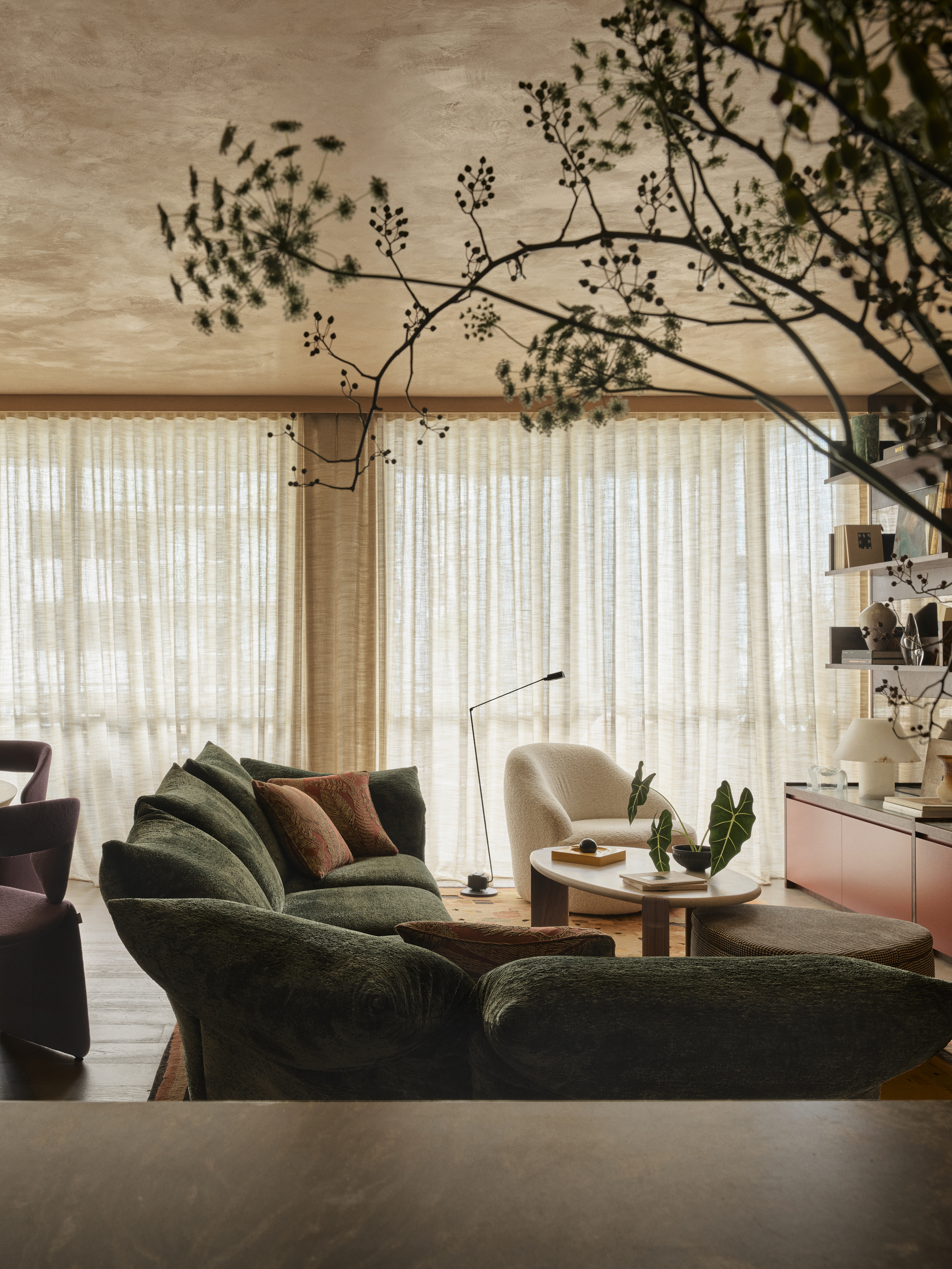 green edra standard sofa in a modern living room with rendered ceiling, sheer blinds, accent chair with nesting tables, thin floor lamp