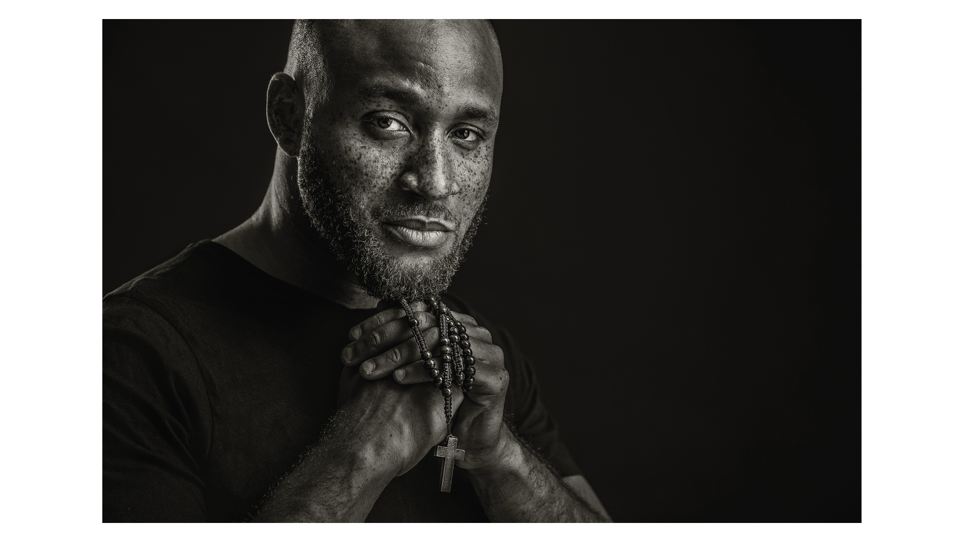Winning entry of the BIPP International Print Masters competition 2021 – a black and white photo of a man clutching a rosary, photographed by Gary Hill