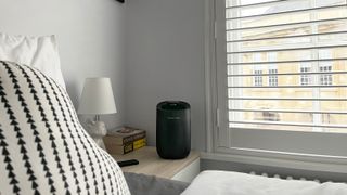 small black dehumidifier on bedside table next to windows with white shutters