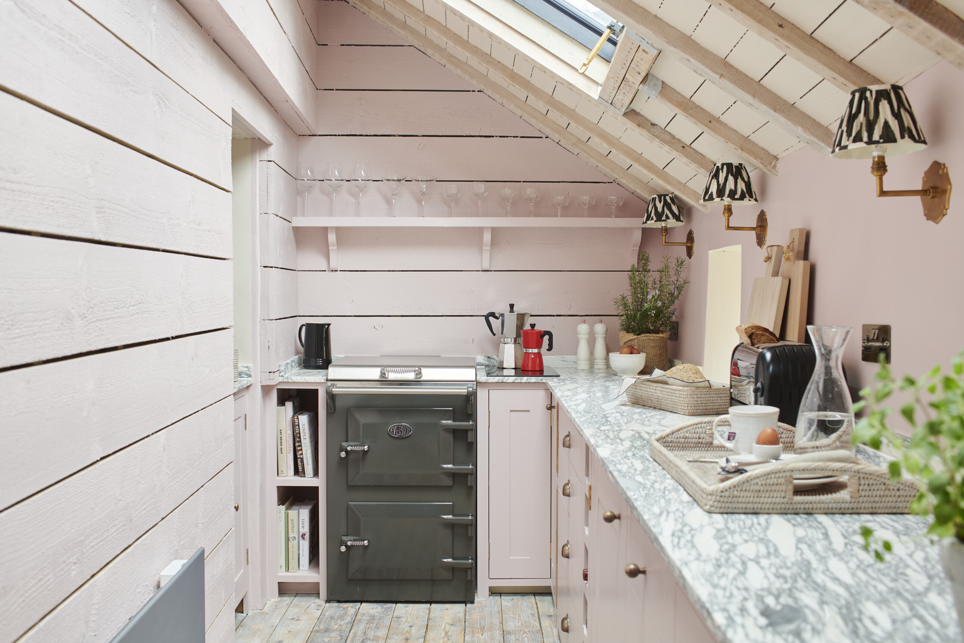 A small and narrow pink kitchen with shiplap on the walls and a sloped roof with roof lights