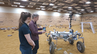 Tom Scott steering a Mars rover prototype with a modified Steam Deck. An Airbus engineer looks on.