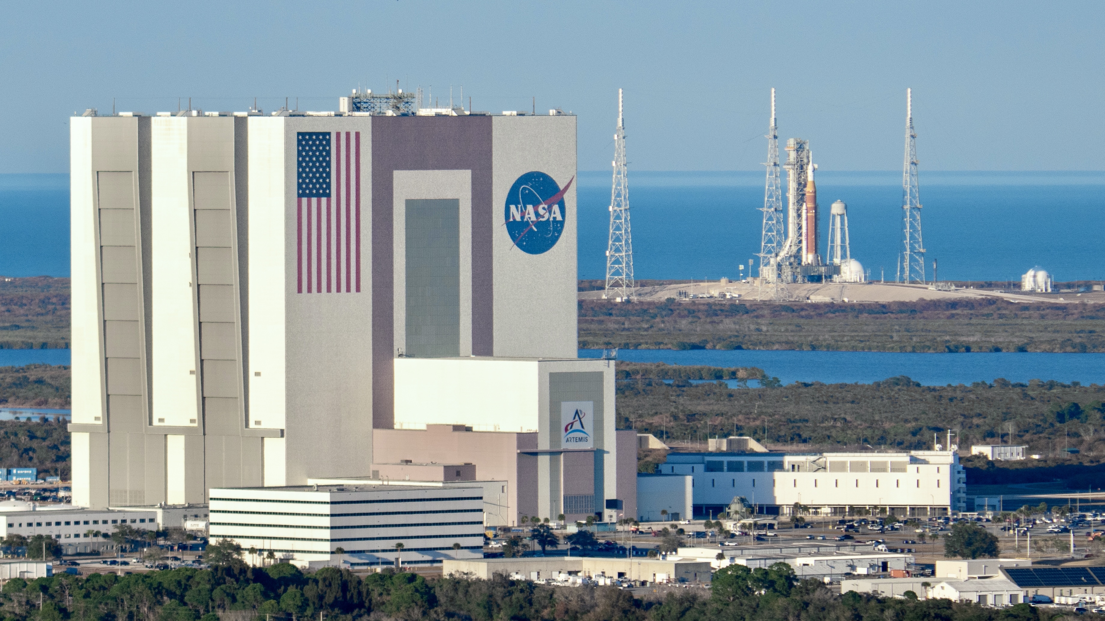 A bit orange rocket stands behind a giant white building.
