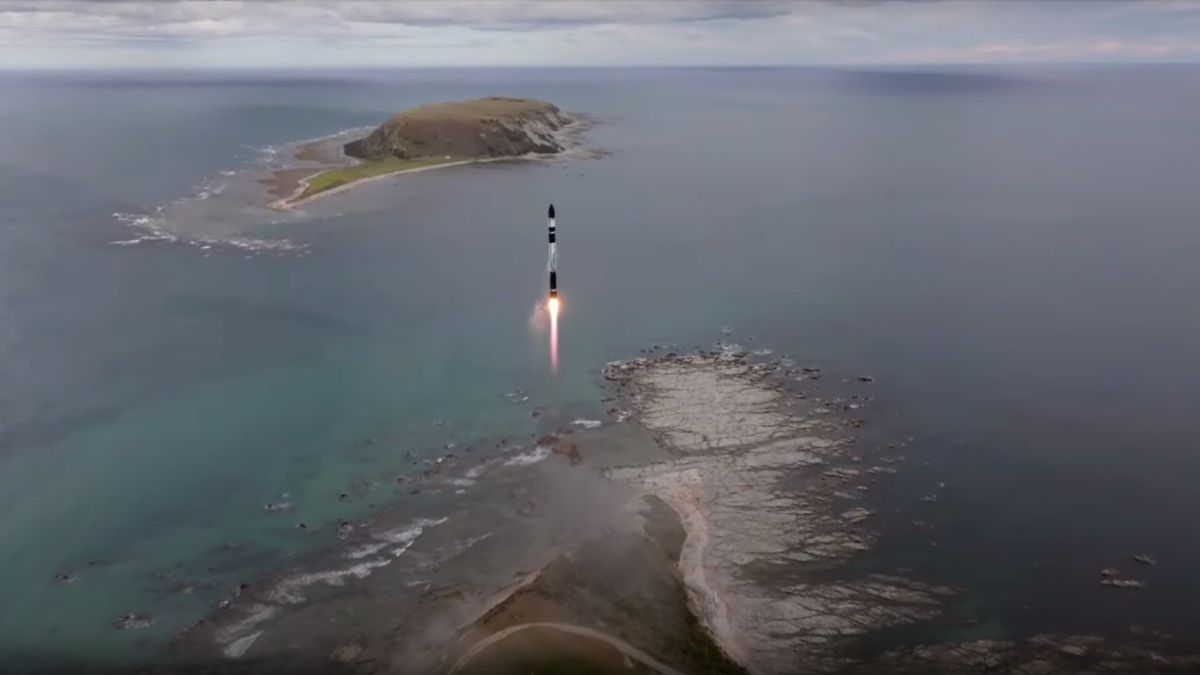 a small black and white rocket launches into the sky from a seaside pad