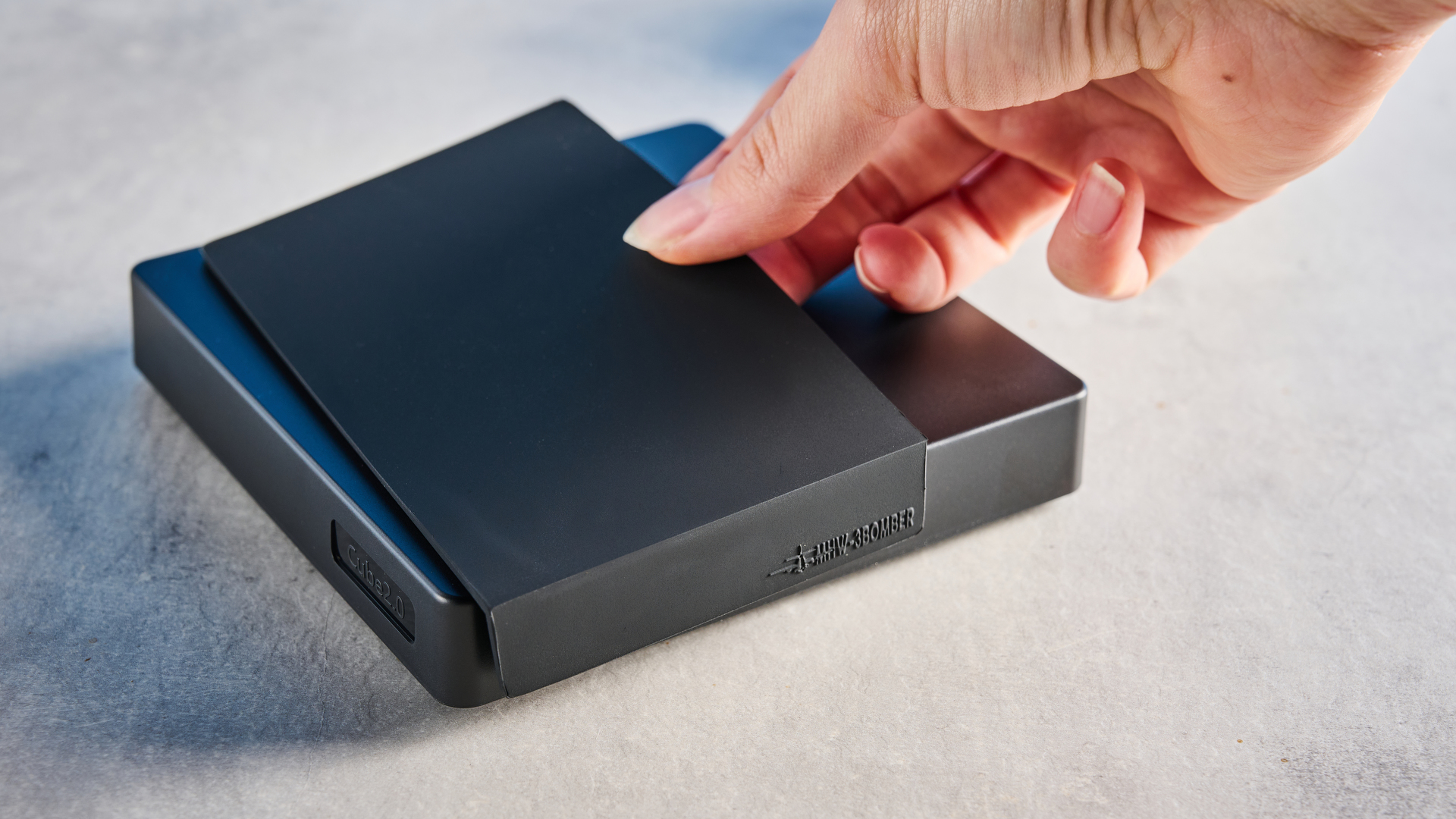 the mhw-3bomber cube coffee scale 2.0 in black photographed against a blue background showing its button controls and dial surface