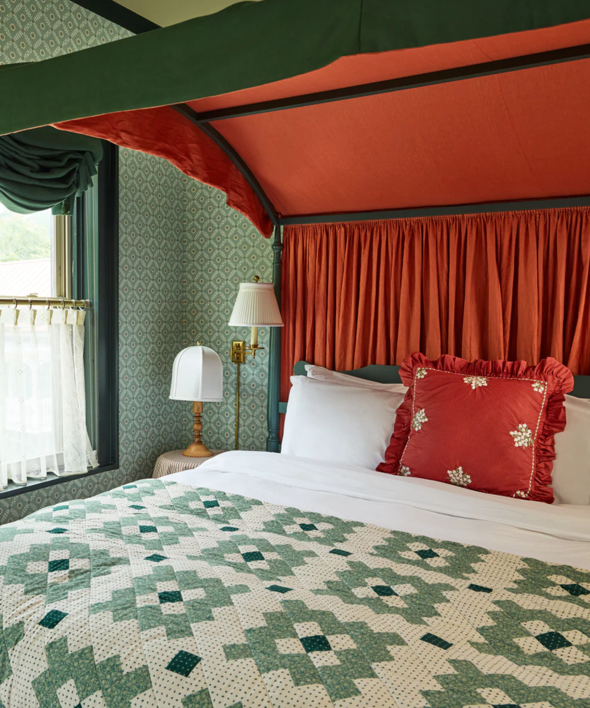 a bed with a green quilt and a red pillow