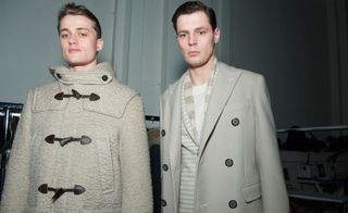 Two male models wearing looks from Canali's collection. They are wearing cream and grey coats, a striped jacket and a white crew neck top