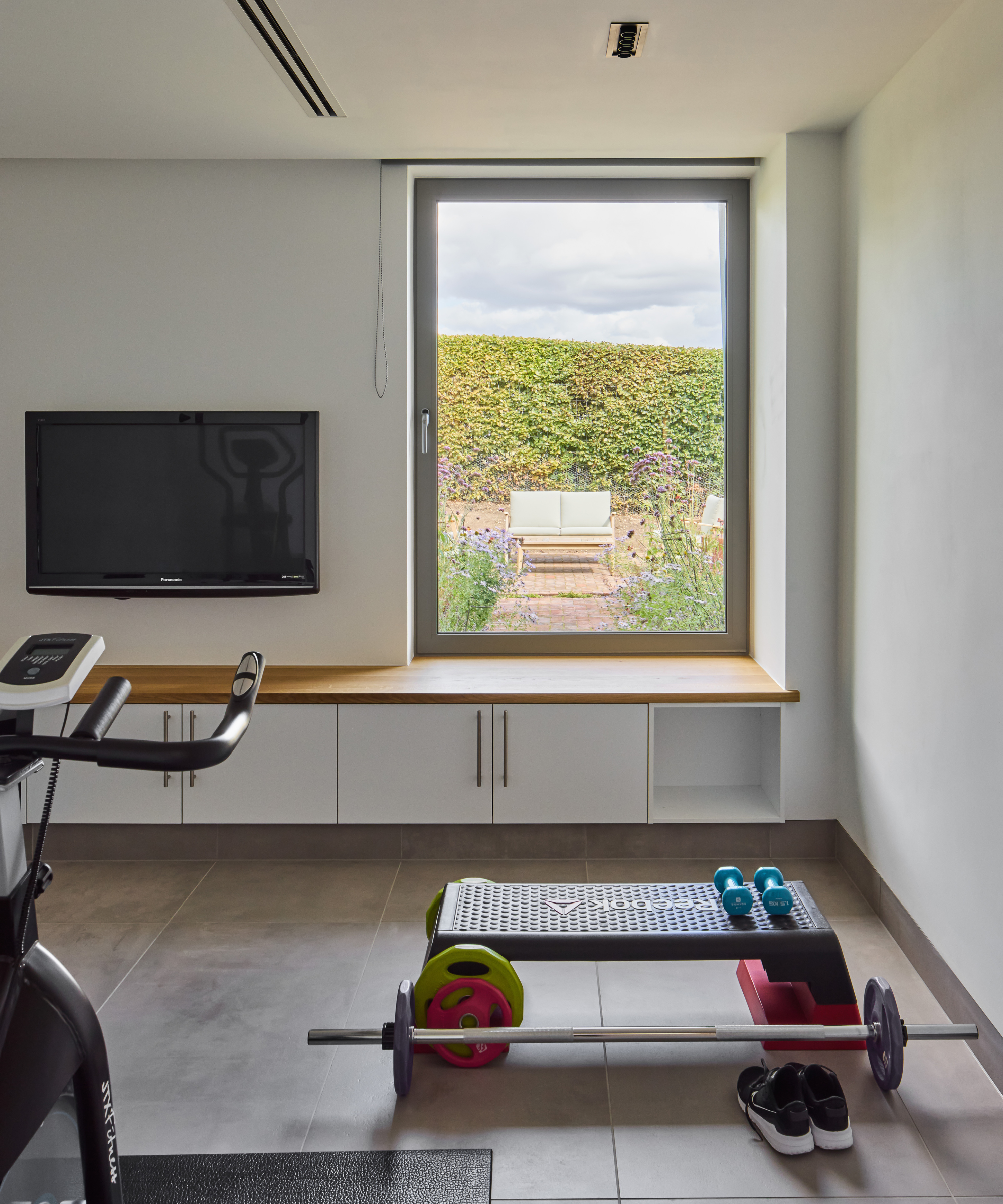 Home gym with weights and a cabinet seat under window overlooking garden