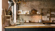 A Manhattan apartment kitchen with exposed stone walls, blue dark blue wood cabinetry, and open shelves filled with wood cutting boards and framed art