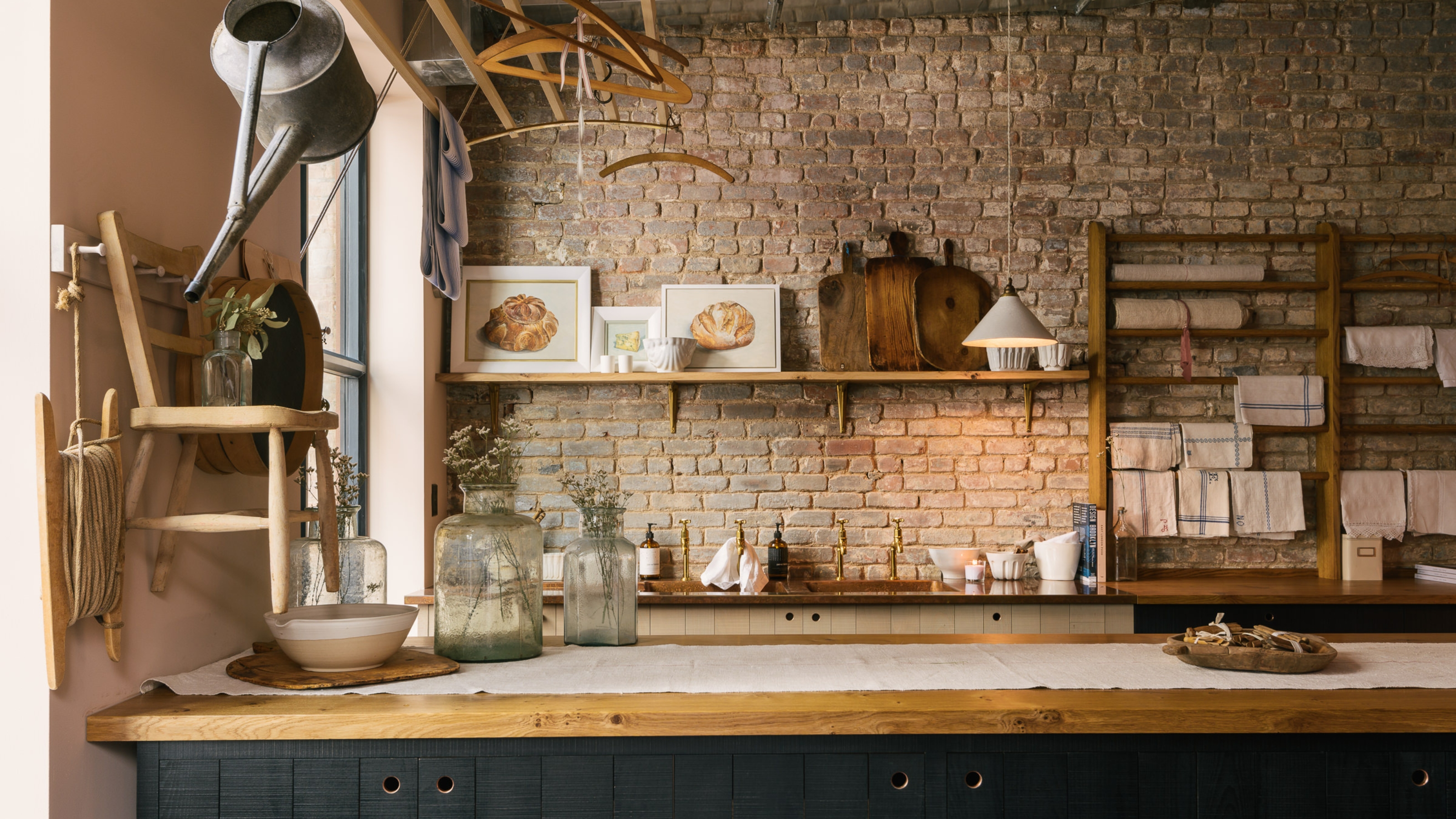 A Manhattan apartment kitchen with exposed stone walls, blue dark blue wood cabinetry, and open shelves filled with wood cutting boards and framed art