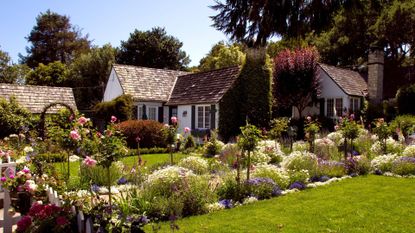 Various cottage garden ideas shown on a real-life yard including a white picket fence, colorful planting and rose arbours