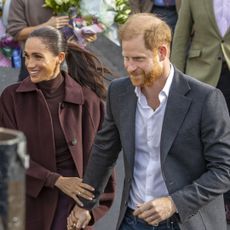 Meghan Markle wearing a maroon coat holding Prince Harry's arm