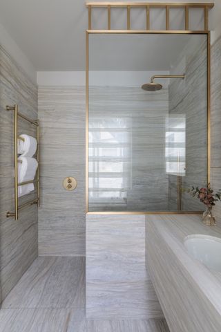 An example of spa bathroom ideas showing a neutral colored stone floor and wall tiles with gold fixtures and fittings