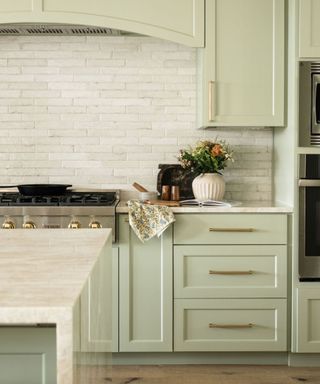 kitchen with light green cabinets, white textured wall tiles with cozy rustic decor on countertops