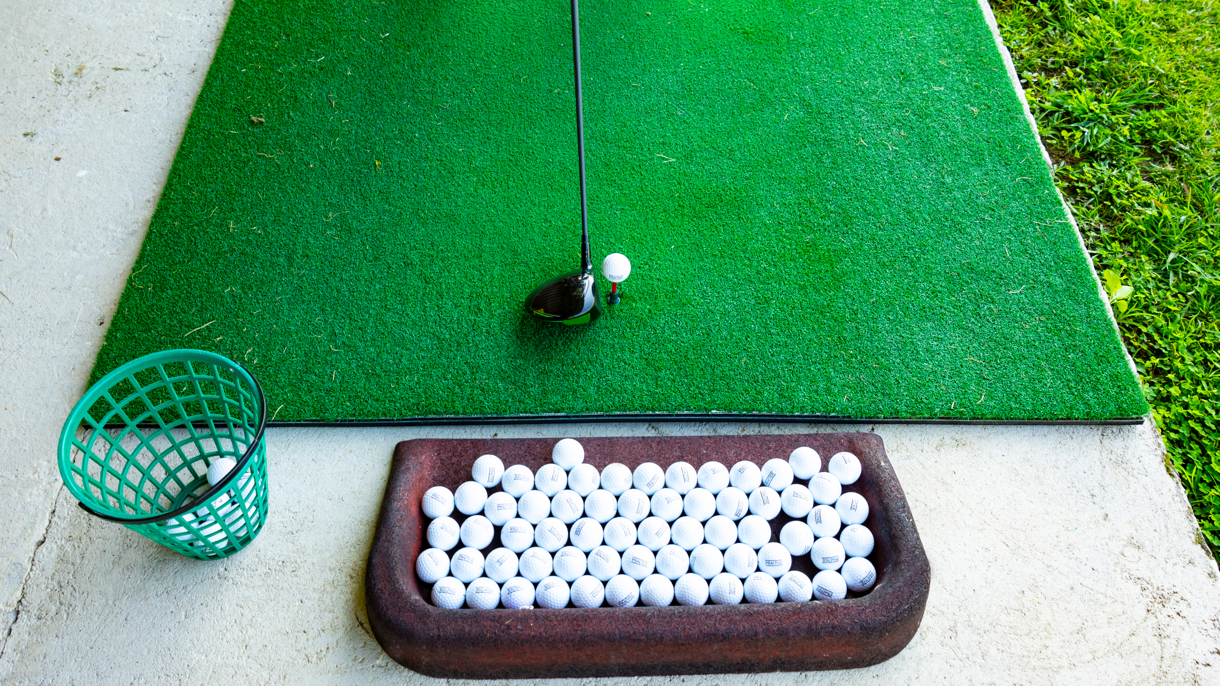 A driver head behind a ball at the driving range