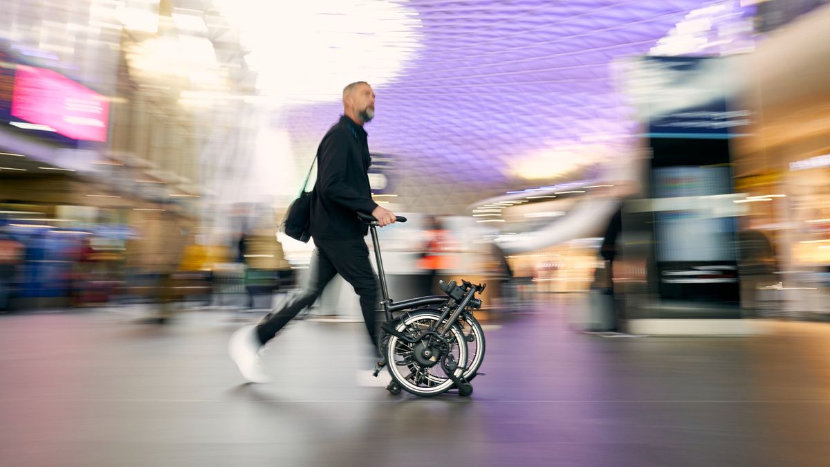 Brompton Electric P Line, folded and being wheeled using the roller rack through King’s Cross train station in London