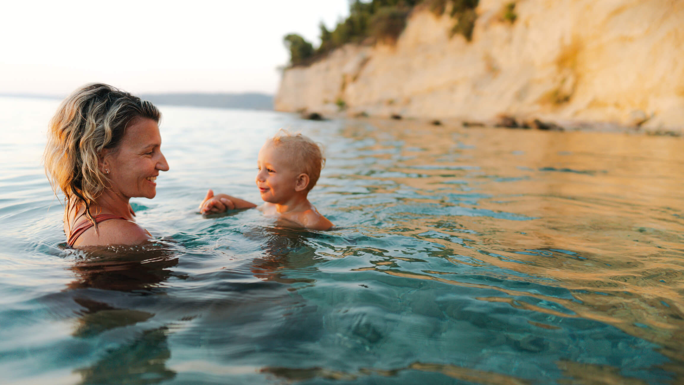 A mother is swimming in the open water with her child.