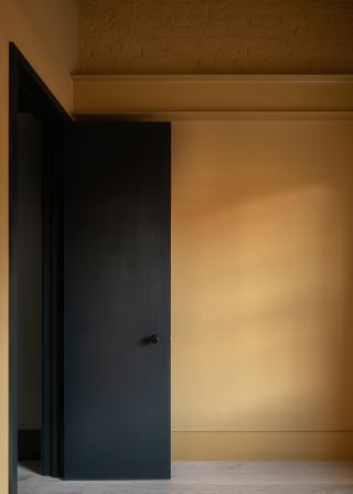 Dark door and yellow walls at private rooms upstairs at Concrete Plinth House by DGN studio