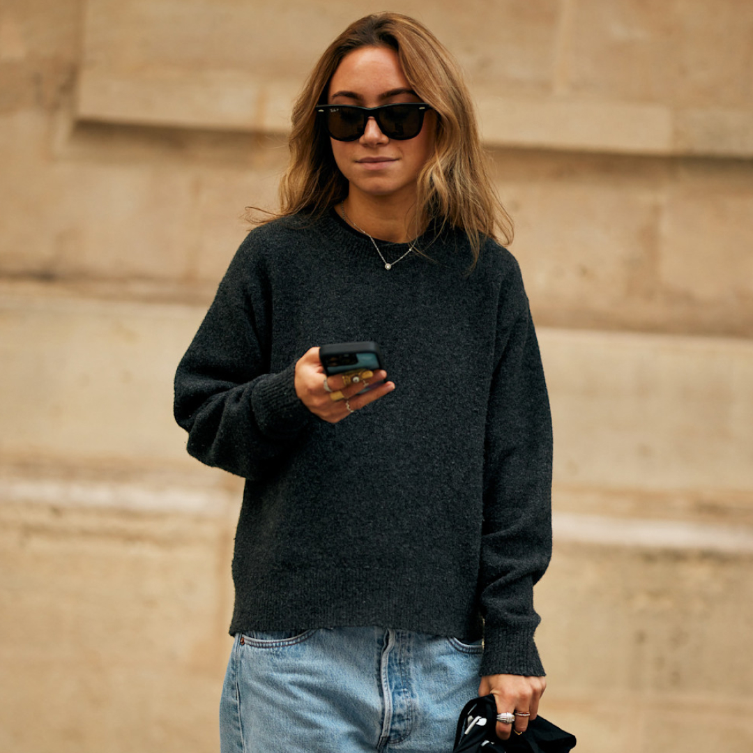 fashion week attendee wearing sunglasses and grey sweater holding phone