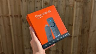 Amazon Fire TV Stick 4K boxed held in front of a wooden background