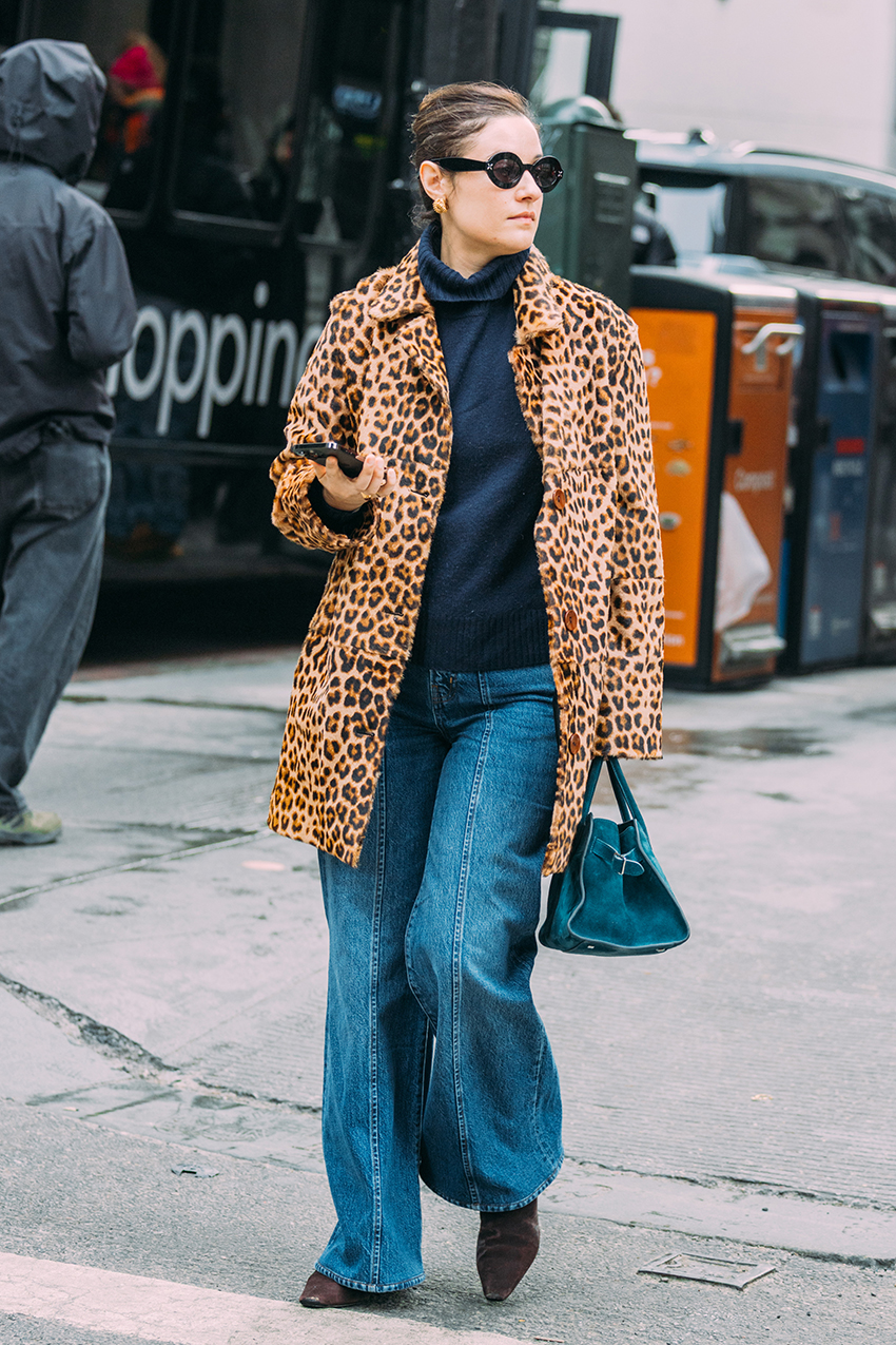 A woman wearing a cheetah coat, black turtleneck, jeans, and pointed toe heels