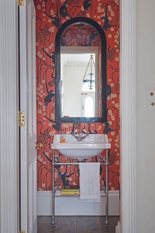 Powder room with red stylised wallpaper, black mirror, white vanity