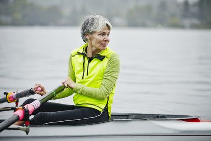 A fit, senior woman looks over her shoulder as she rows a boat.