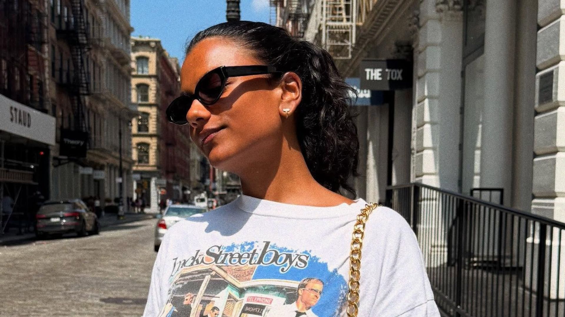 Actor Simone Ashley wears a graphic t-shirt with denim shorts, a leather bag and a black leather belt.