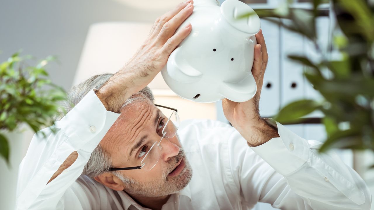 A man holds an empty piggy bank upside down, looking for money to fall out.