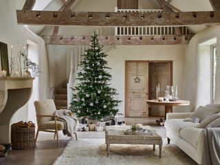 farmhouse style Christmas living room with neutral scheme, fluffy rugs, beams, white decorations on tree, candles, neutral gift wrapping