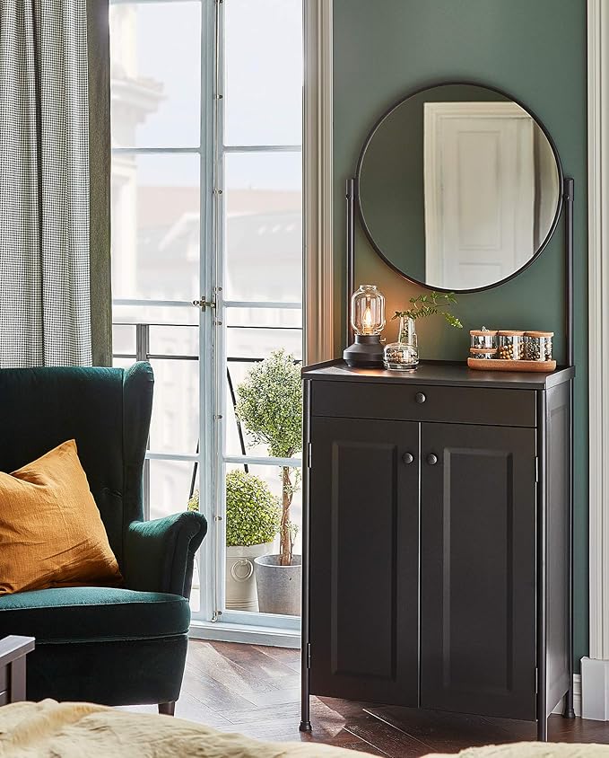 Table lamp on anthracite mirror sideboard in dark green room with dark green chair winged armchair and plain ochre yellow cushion
