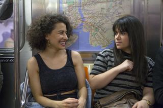 abby and ilana smile at each other while riding on the subway in broad city