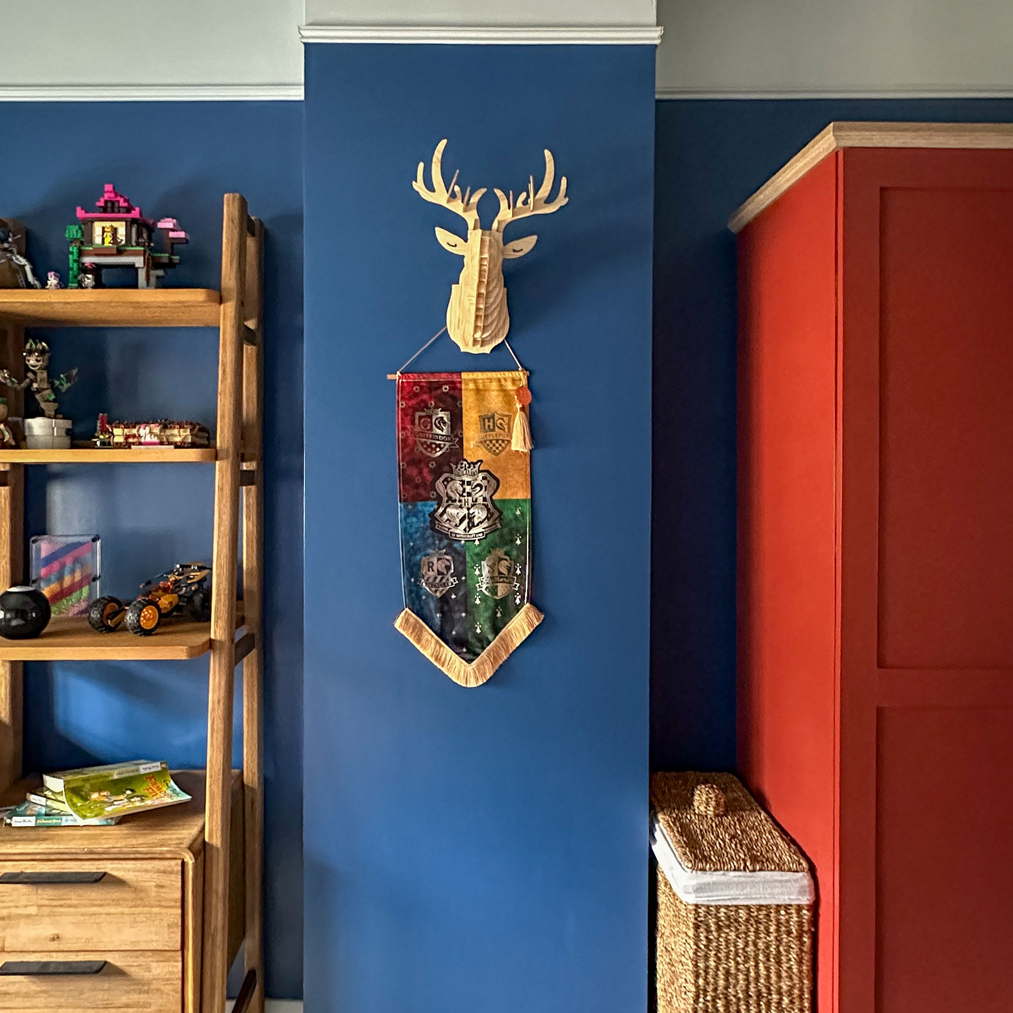 Blue boys room with wooden furniture, red wardrobe, deer head style wall decoration and Harry Potter wall hanging