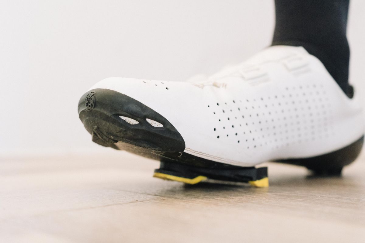 A close up of a white cycling shoe with a black socked foot in it