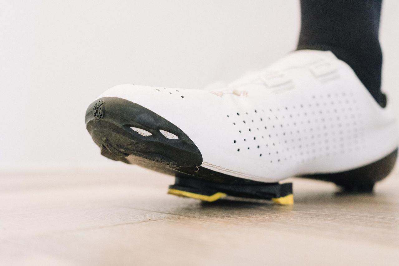 A close up of a white cycling shoe with a black socked foot in it