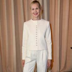 Kelly Rutherford poses for a photo wearing white trousers with beige heels and a white jacket.