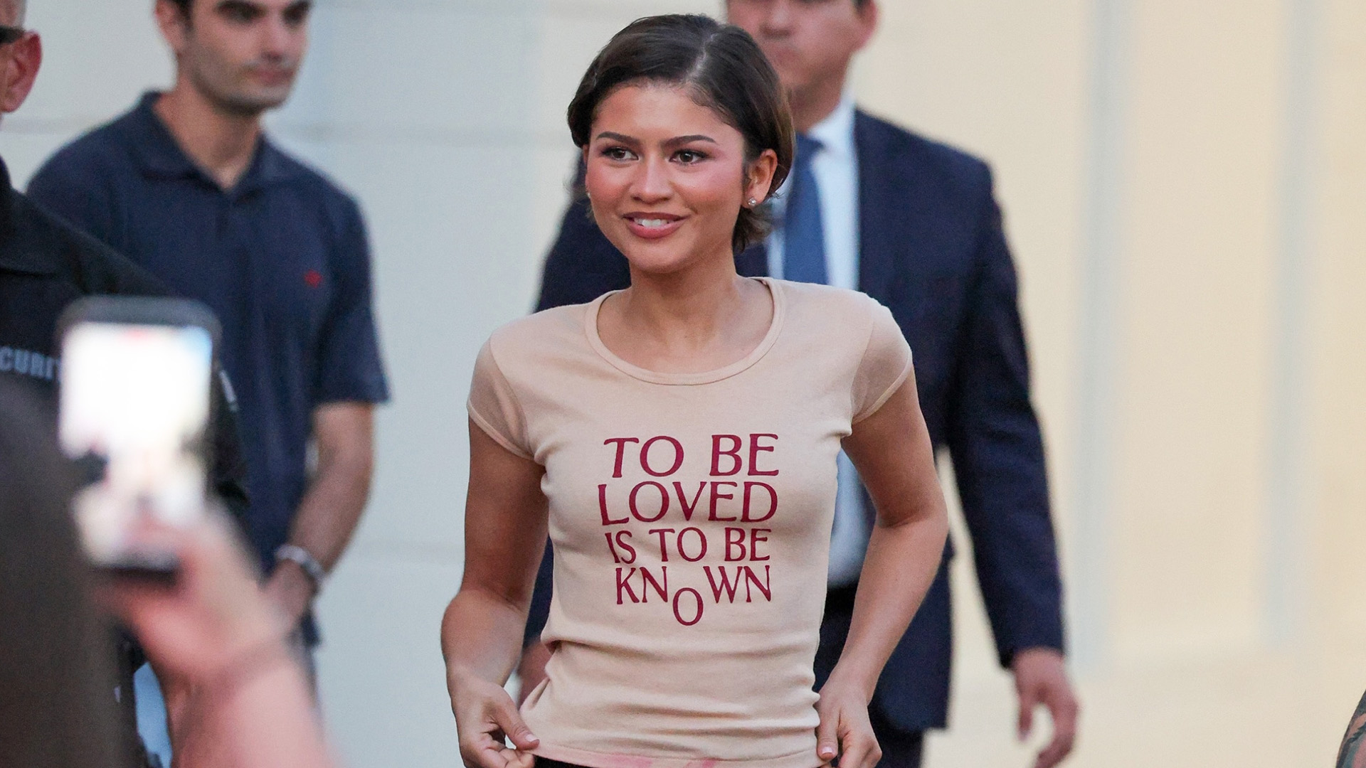 Zendaya wearing a The Drama T-shirt, lace-trim pencil skirt, and red loafers