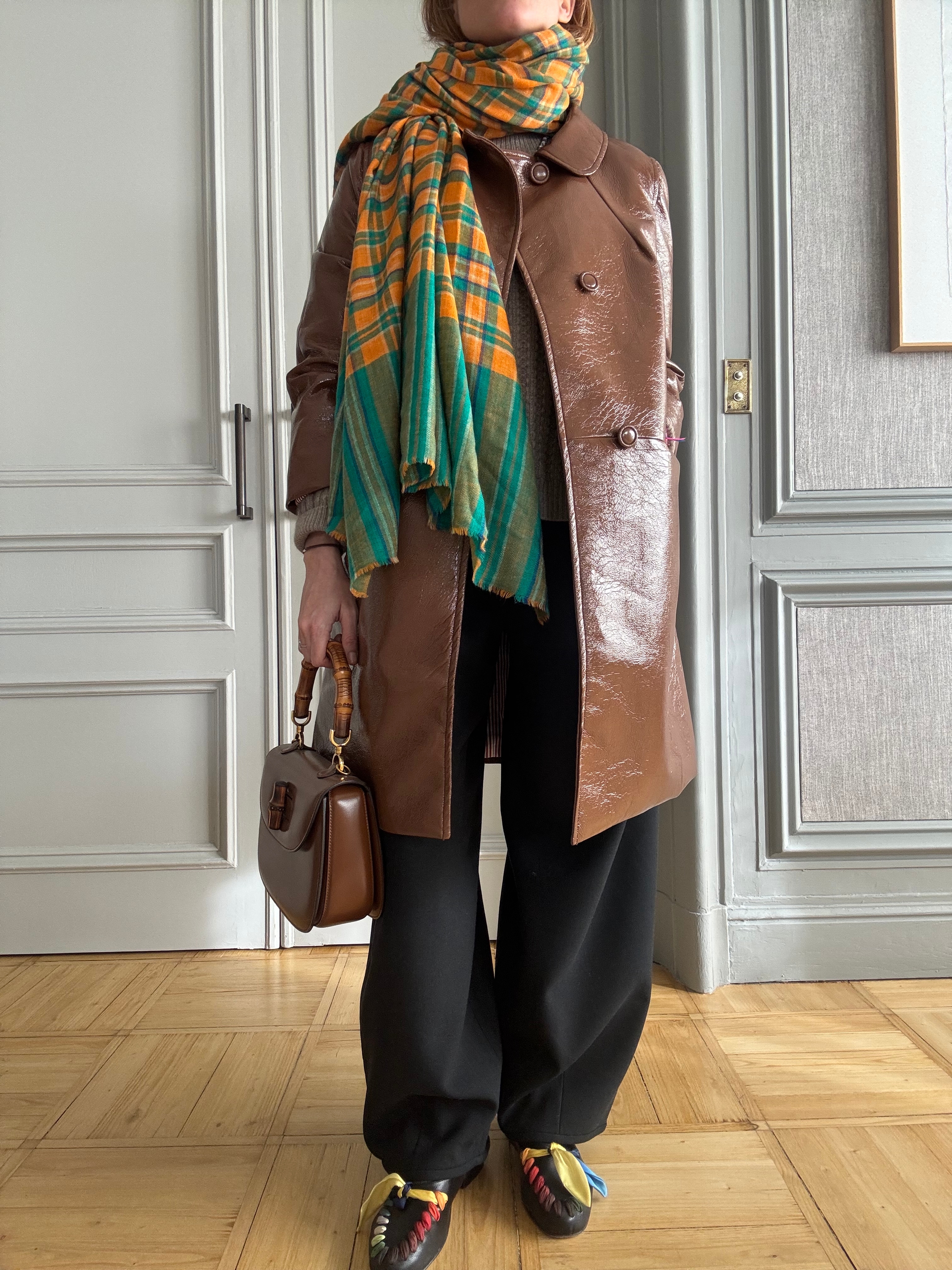 blanca miro wears a brown patent jacket, black baggy trousers, multicoloured trainers and a green and orange scarf.